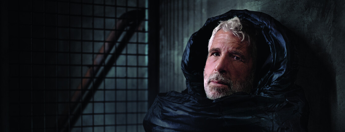 Der Fernsehmoderator Dirk Stermann als Obdachloser im Schlafsack abgebildet